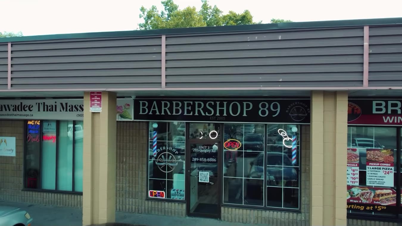 The Barbershop 89 storefront at 205 Quigley Road: black sign, barber poles and the open sign in the window