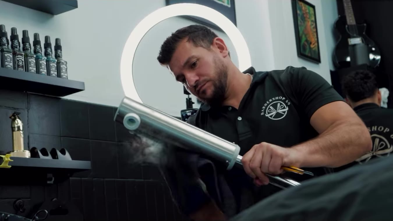 A barber preparing a steaming hot towel under the ring light
